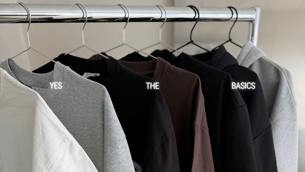 A clothing rack displaying multiple sweatshirts in different colors, labeled with white text overlays 'YES', 'THE', 'BASICS'.